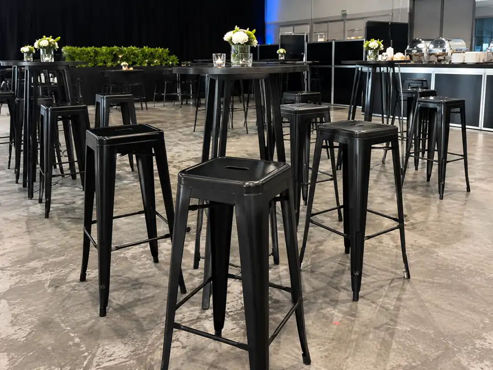 Black Tolix bar stools close up beside high cocktail tables
