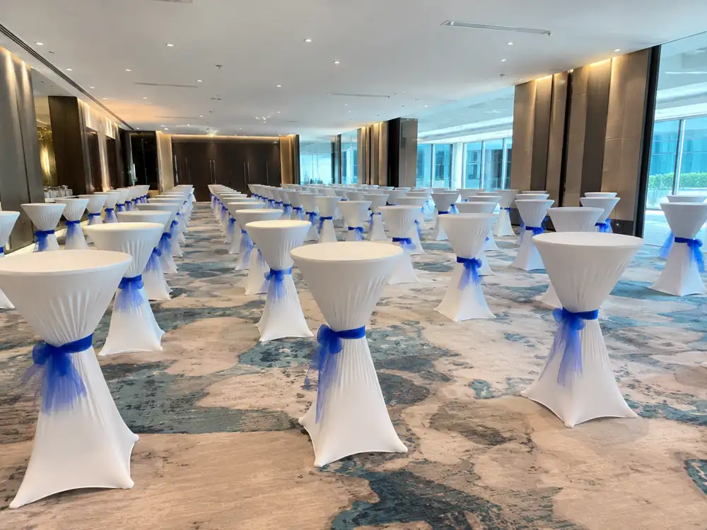 Wide ballroom view with white cocktail tables and blue sash accents