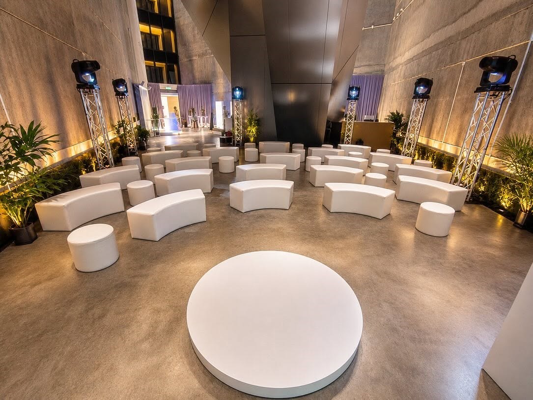White curved lounge benches and round ottomans arranged in a modern event foyer